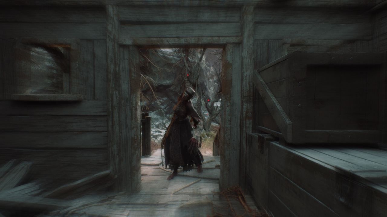 A demonic looking figure, smartly dressed, stands in a cabin's open doorway, looking in toward the viewer.