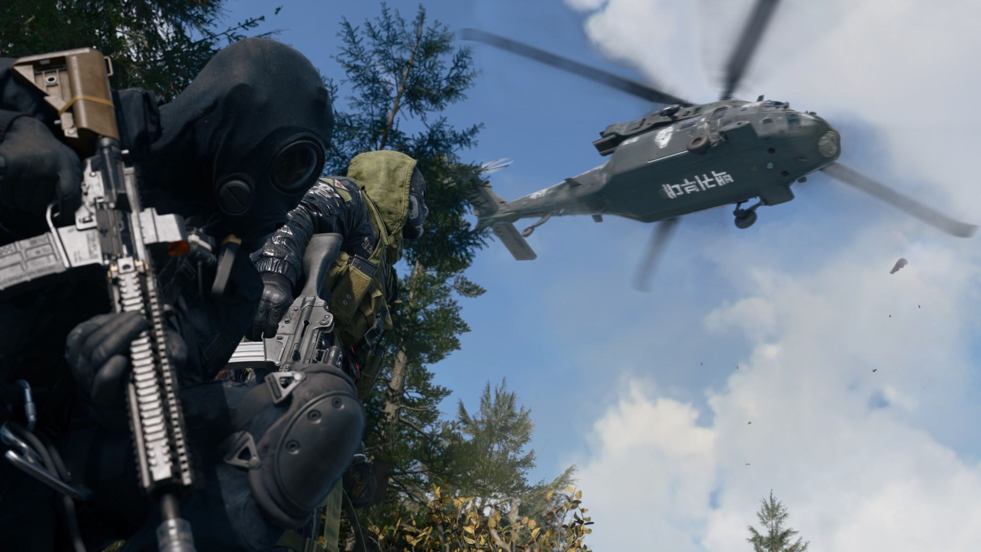 Two soldiers carrying rifles look up at a line of trees as a helicopter flies into view overhead.